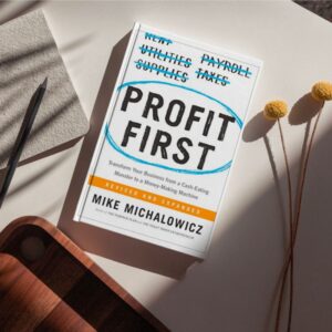 A compelling book cover featuring the title "Profit First" in bold, impactful letters against a backdrop of currency symbols and financial charts. The cover design signifies the importance of prioritizing profits and financial success in business. It conveys the idea of taking control of finances and adopting a strategic approach to profitability.